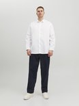 Man draagt een wit Jack & Jones overhemd en donkere jeans.
