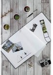 Open grijs album op een houten achtergrond met plantjes, een pen en een camera.