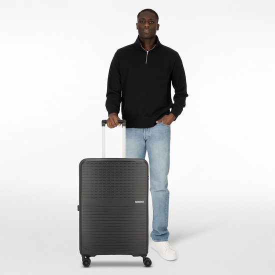 Een man met een zwarte koffer met geribbelde textuur, TSA-slot en vier wielen.