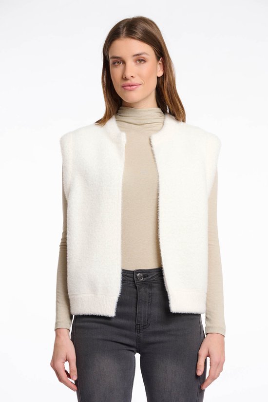 Wit fluffy vest met ronde hals, gedragen over een beige coltrui en grijze jeans.