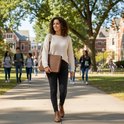 Vrouw met een bruine leren schrijfmap op een universiteitscampus.