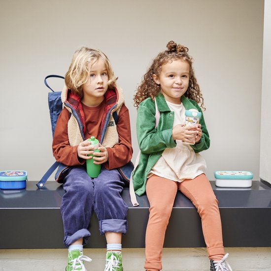 Deux enfants, un garçon avec une gourde verte et une fille avec une tasse à motif dinosaure, sont assis dehors.