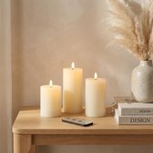 Drie crèmekleurige, gladde LED-kaarsen van echt was met realistische vlammen, op een houten tafel met afstandsbediening en pampasgras.