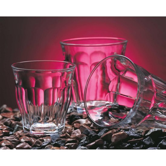 Trois verres, dont un couché, remplis de boissons rouges et bleues et posés sur des pierres.