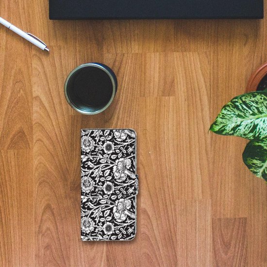 Zwart telefoonhoesje met bloemenpatroon op een houten bureau, naast een mok en pen.