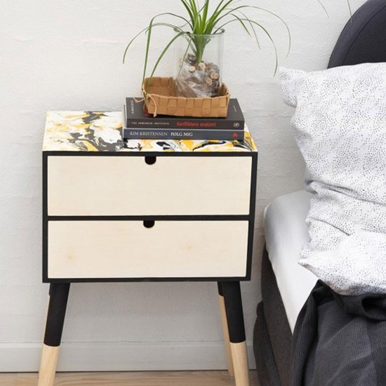 Nachtkastje met zwart frame, twee lichte houten lades en een marmerlook blad in geel, zwart en wit.