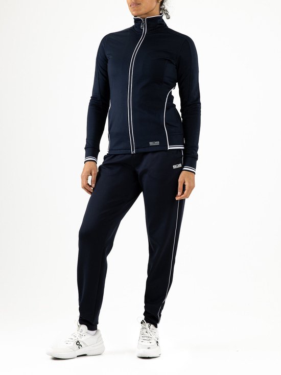 Model in een volledig donkerblauw trainingspak. Het jack heeft een witte bies en de broek heeft een witte bies langs de pijpen. Merk: Sjeng Sports.