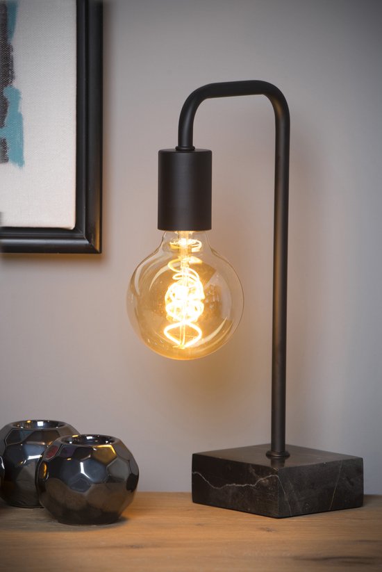 Une lampe de table moderne noire avec une ampoule Edison ronde, posée sur une base en marbre à côté d'objets décoratifs.