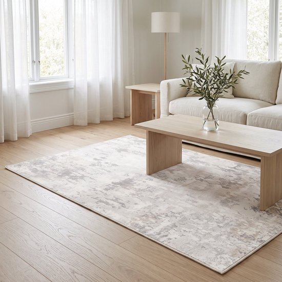 Crèmekleurig vloerkleed met abstract patroon, in een woonkamer met een lichte stoffen bank en houten salontafel.