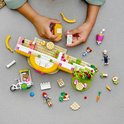 Kinderhanden bouwen aan de LEGO Friends café set. Een foodtruck, café en miniatuur groenten zijn verspreid over een grijze achtergrond.