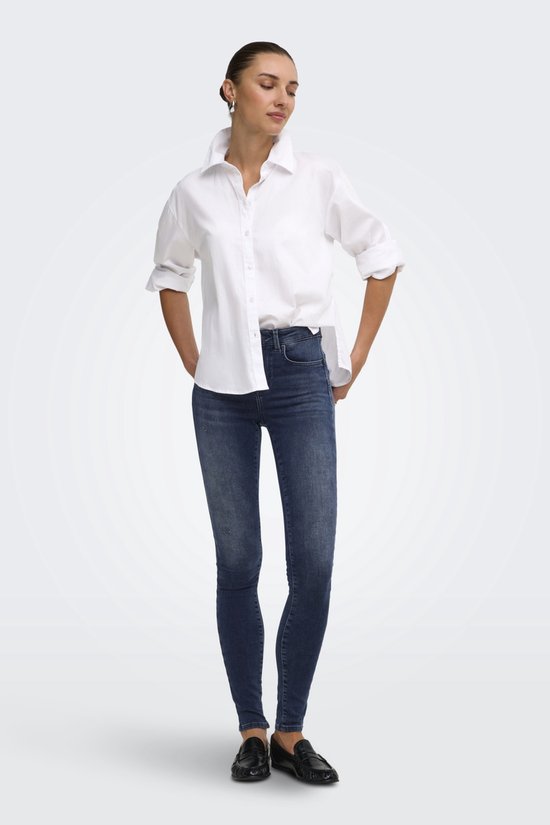 Model draagt een blauwe push-up skinny jeans en een wit overhemd met opgerolde mouwen.