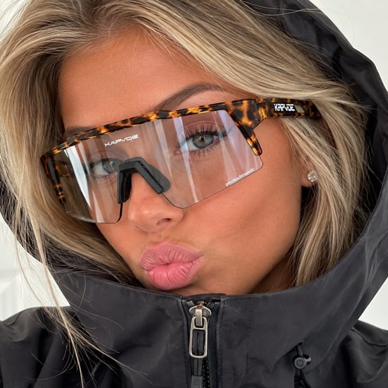 Vrouw met blonde haren en zwarte capuchon draagt KAPVOE sportbril met panterprint montuur en heldere fotochromatische lens.