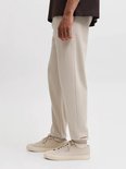 Zijaanzicht van een model in beige sweatpants met elastische boorden en bijpassende sneakers.