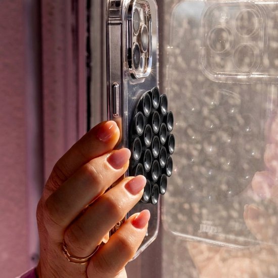 Hand houdt doorzichtige telefoon met zwarte ronde zuignapsticker tegen een raam.