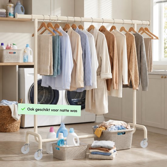Crème kledingrek in een wasruimte volgehangen met kledingstukken en handdoeken, met wasmanden onderaan.