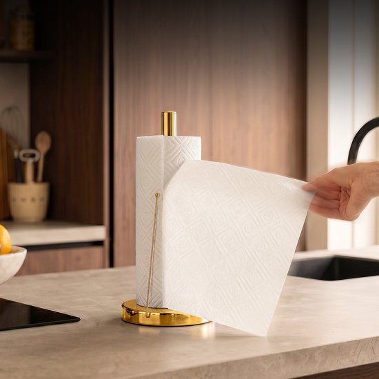 Een hand trekt een vel keukenpapier van de glanzend gouden keukenrolhouder.