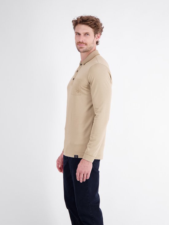 Man in beige poloshirt met lange mouwen, gedraaid naar de zijkant, donkerblauwe broek.