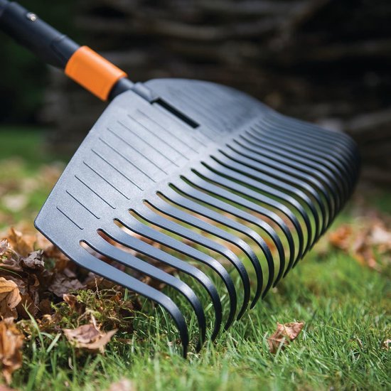 Zwarte bladhark met oranje steel, op gras met bladeren.
