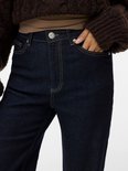 Detail van de donkerblauwe wijde jeans met gele stiksels en knoopsluiting.