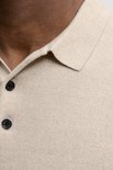 Close-up van de kraag en knopen van een beige gebreide polo.