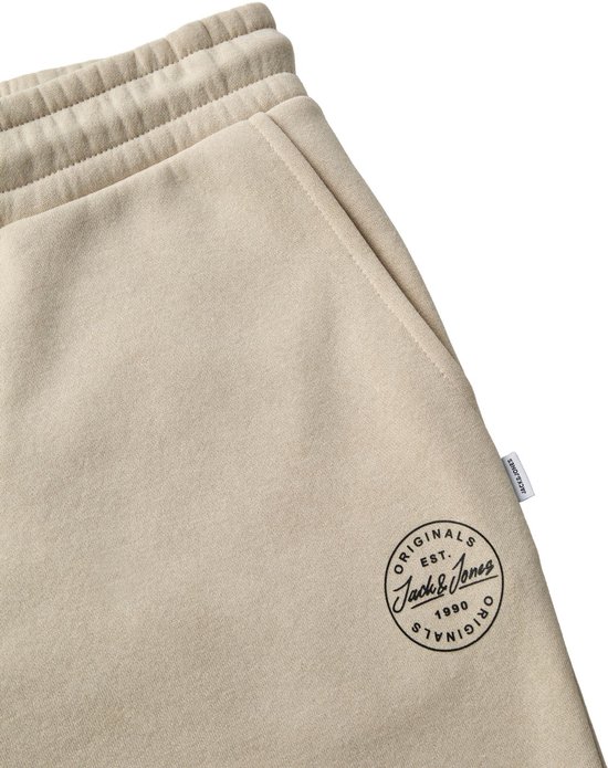 Close-up van beige Jack & Jones joggingbroek met rond Originals logo en klein merklabel aan de zijnaad.