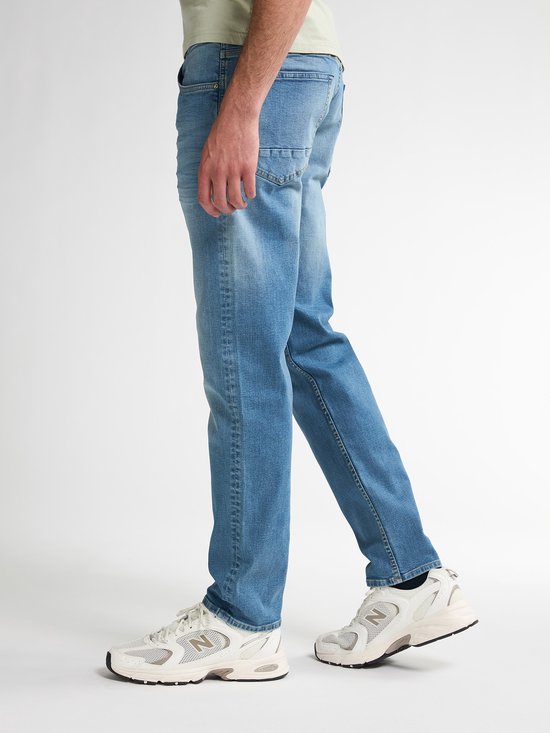 Man met lichtblauwe jeans met een regular tapered fit en beige sneakers.