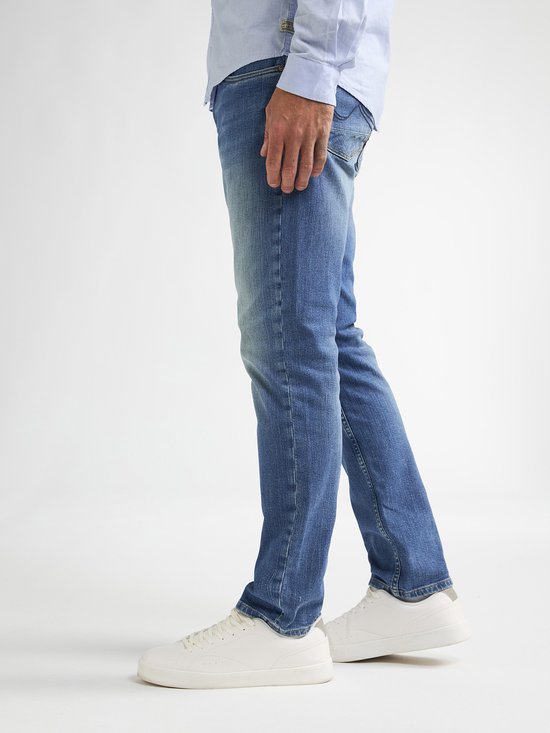 Model draagt een blauwe straight fit spijkerbroek van Petrol Industries met witte sneakers.
