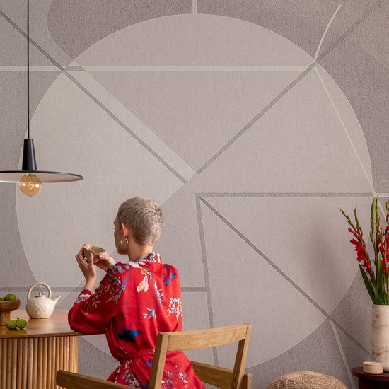 Persoon in rode kimono voor een grijze muur met geometrisch patroon en een moderne hanglamp.