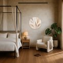 Ronde wandcirkel met abstracte bladeren in beige en goudtinten, geplaatst in een sfeervolle slaapkamer met hemelbed.