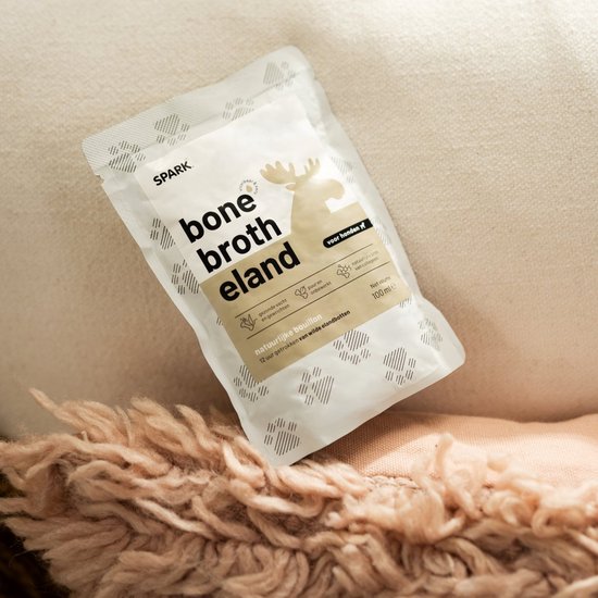 Een zakje SPARK 'bone broth eland' ligt op een zachtroze deken.