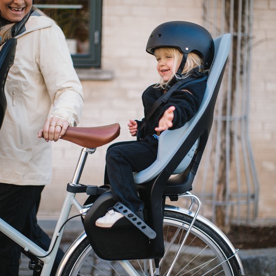 Vrolijk meisje in een lichtblauw fietsstoeltje op een fiets, met een vrouw ernaast.