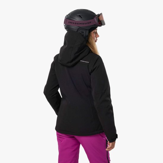 Zwarte ski-jas, gedragen door een vrouw met paarse skibroek en helm, zicht van achteren.