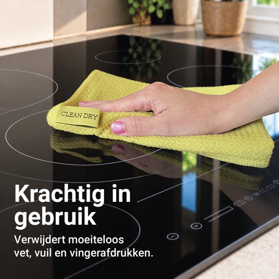 Hand veegt een glanzende kookplaat schoon met een gele Clean Dry microvezeldoek.