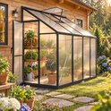 Zwarte kas tegen een houten blokhut, gevuld met planten en een gieter bij zonsondergang.