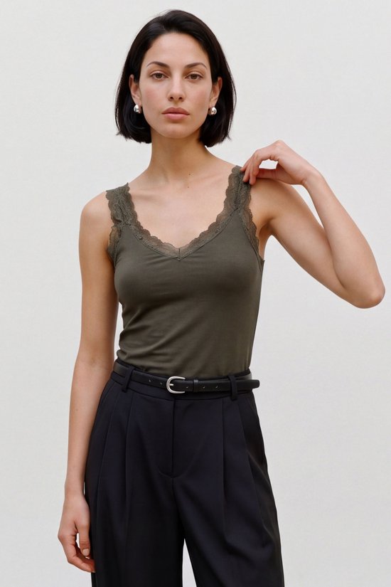 Model draagt een olijfgroene VERO MODA top met kanten schouderbandjes en V-hals, gecombineerd met een zwarte pantalon.