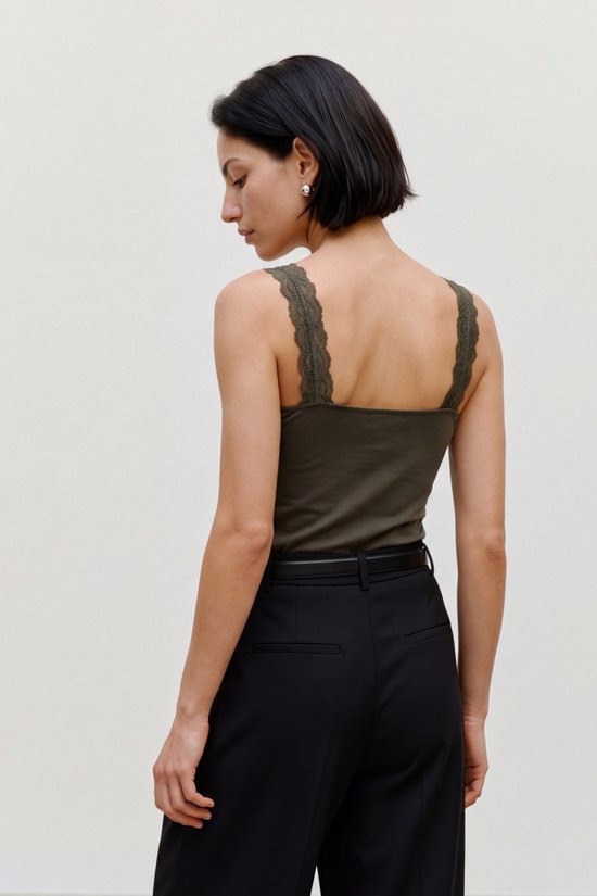 Achterkant van de olijfgroene VERO MODA top met kanten details op de schouderbandjes, gedragen op een zwarte pantalon.