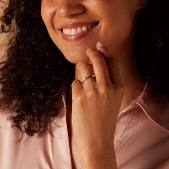Gezicht van een lachende vrouw die met haar vinger naar een zilverkleurige ring met zirkonia wijst.