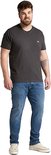 Grote man met een donkergrijs T-shirt en een lichtblauwe jeans, staand met handen in de zakken.