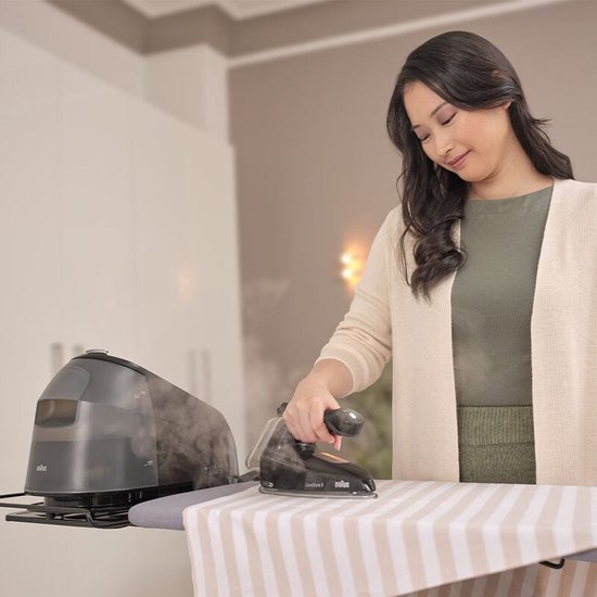 Vrouw met beige vest strijkt met zwart Braun CareStyle 5 strijkijzer. Grijze station geeft stoom af.