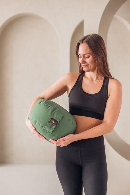 Vrouw met lang bruin haar in sportkleding die een olijfgroen meditatiekussen vasthoudt.