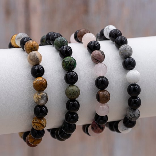 Vier armbanden met verschillende edelsteenkralen, waaronder roze, zwart en bruin.