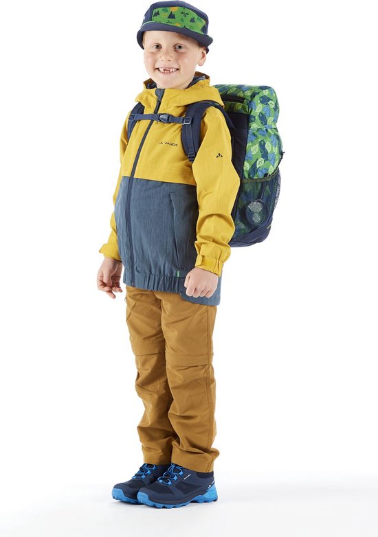 Jongen in gele en blauwe jas, bruine broek, pet en rugzak met groen bladpatroon.