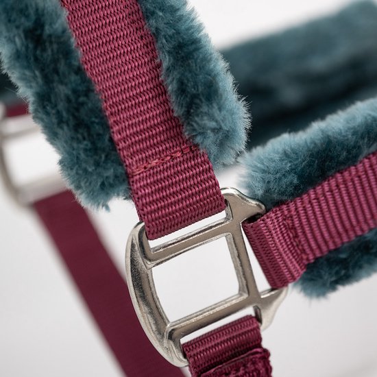 Detailopname van een paardenhalster met bordeauxrode banden en blauwzwarte imitatiebontvoering.