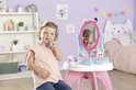 Jong meisje met strik in haar haar zit bij de Gabby's Dollhouse kaptafel en doet make-up op.