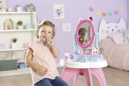 Jong meisje met strik in haar haar zit bij de Gabby's Dollhouse kaptafel en doet make-up op.