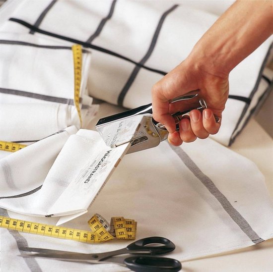 Hand gebruikt zilverkleurige niettang op wit textiel met ruiten en rolmaat.