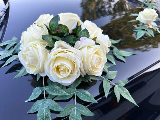 Boeket van crèmegele rozen met groene bladeren, geplaatst op een zwarte auto.