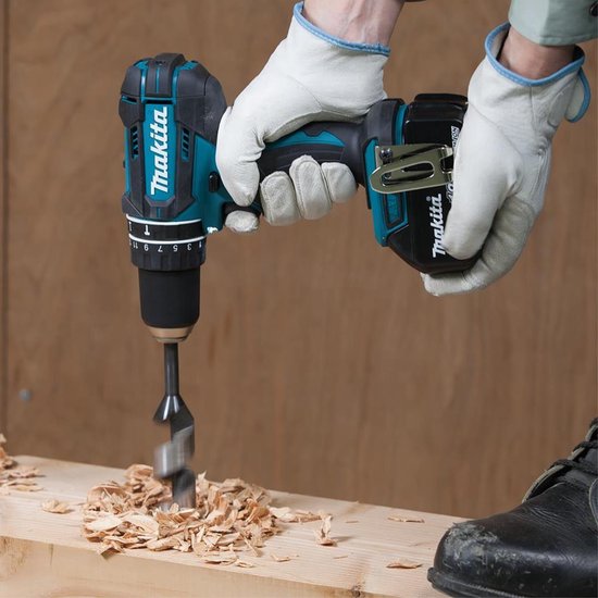 Handen met witte handschoenen gebruiken een turquoise en zwarte Makita accuboormachine om in hout te boren.