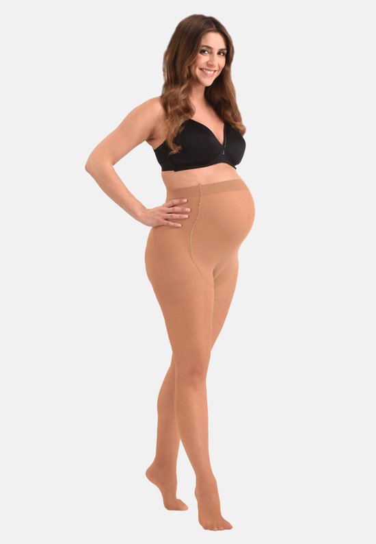 Zwanger model in een zwarte BH en beige, doorschijnende zwangerschapspanty, staand.