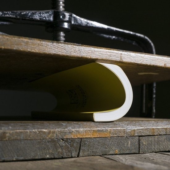Een geel notitieboek in een houten pers, wat de flexibiliteit van de kaft toont.